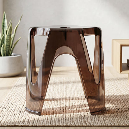 A transparent plastic stool used as a stylish side table next to a sofa.