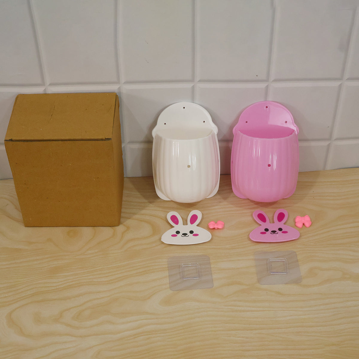 Disassembled white and pink organizers, hooks, and a brown cardboard box on a light wooden surface.
