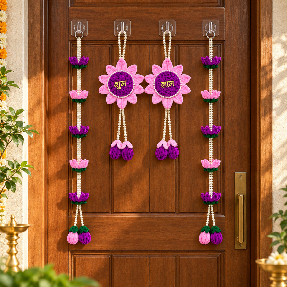 A pair of pink and purple lotus flower hangings and two lotus bead strings on a brown door, with a brass lamp visible.