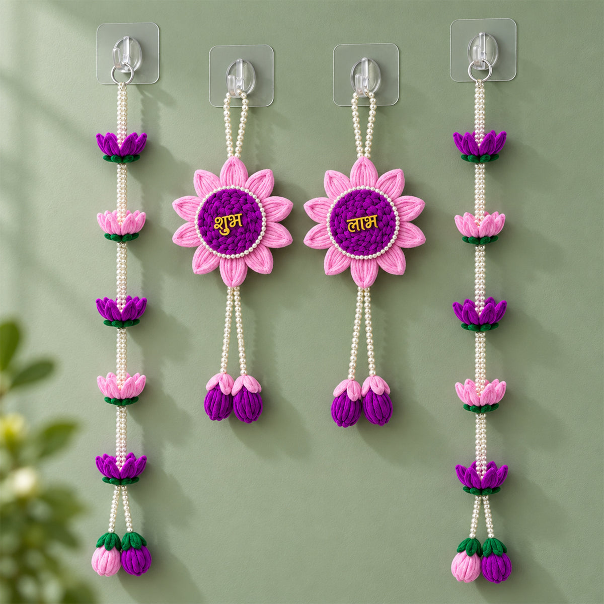 Four pink and purple lotus flower hangings with pearl beads displayed against a light green wall.