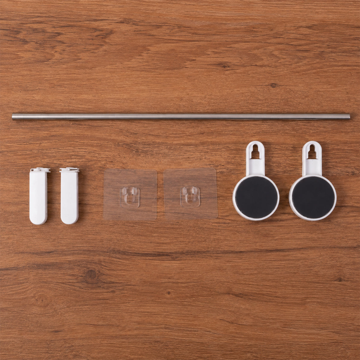 All components of the towel rod set are laid out on a wooden surface: a silver rod, two white end pieces, two clear adhesive
