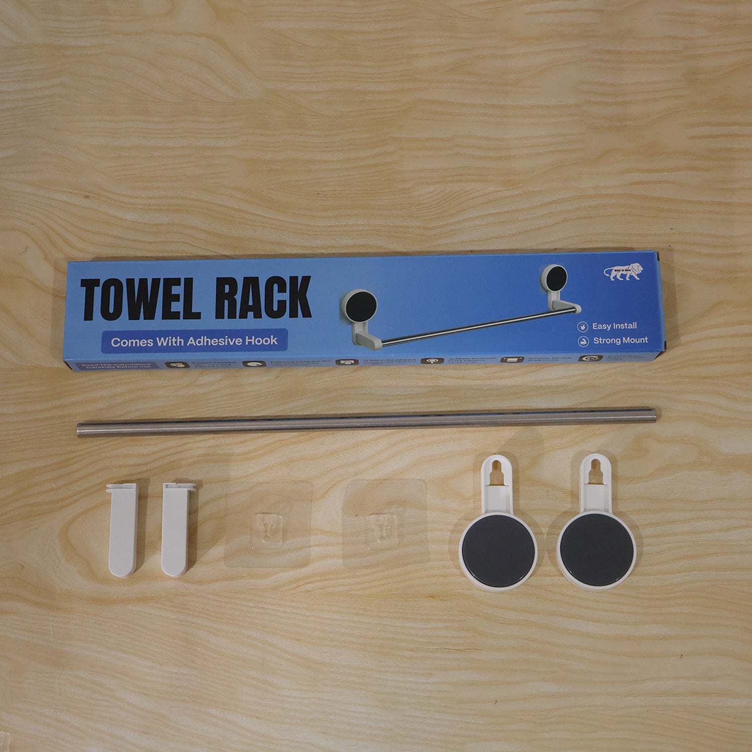 The towel rack packaging and components are laid out on a wooden surface, including the box, rod, end pieces, and hooks.