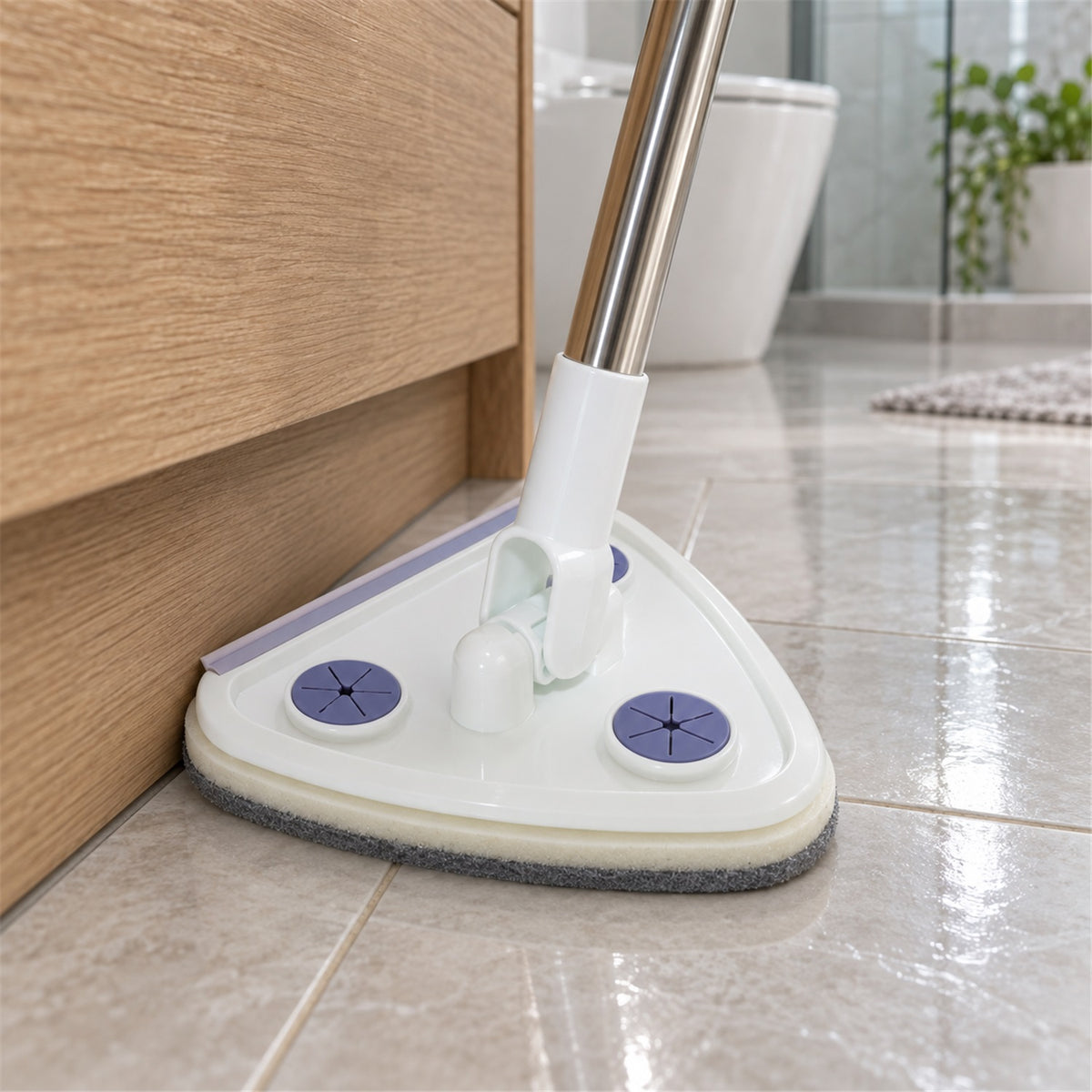Close-up of the white triangular mop head with purple accents, cleaning a tiled floor next to a wooden cabinet.