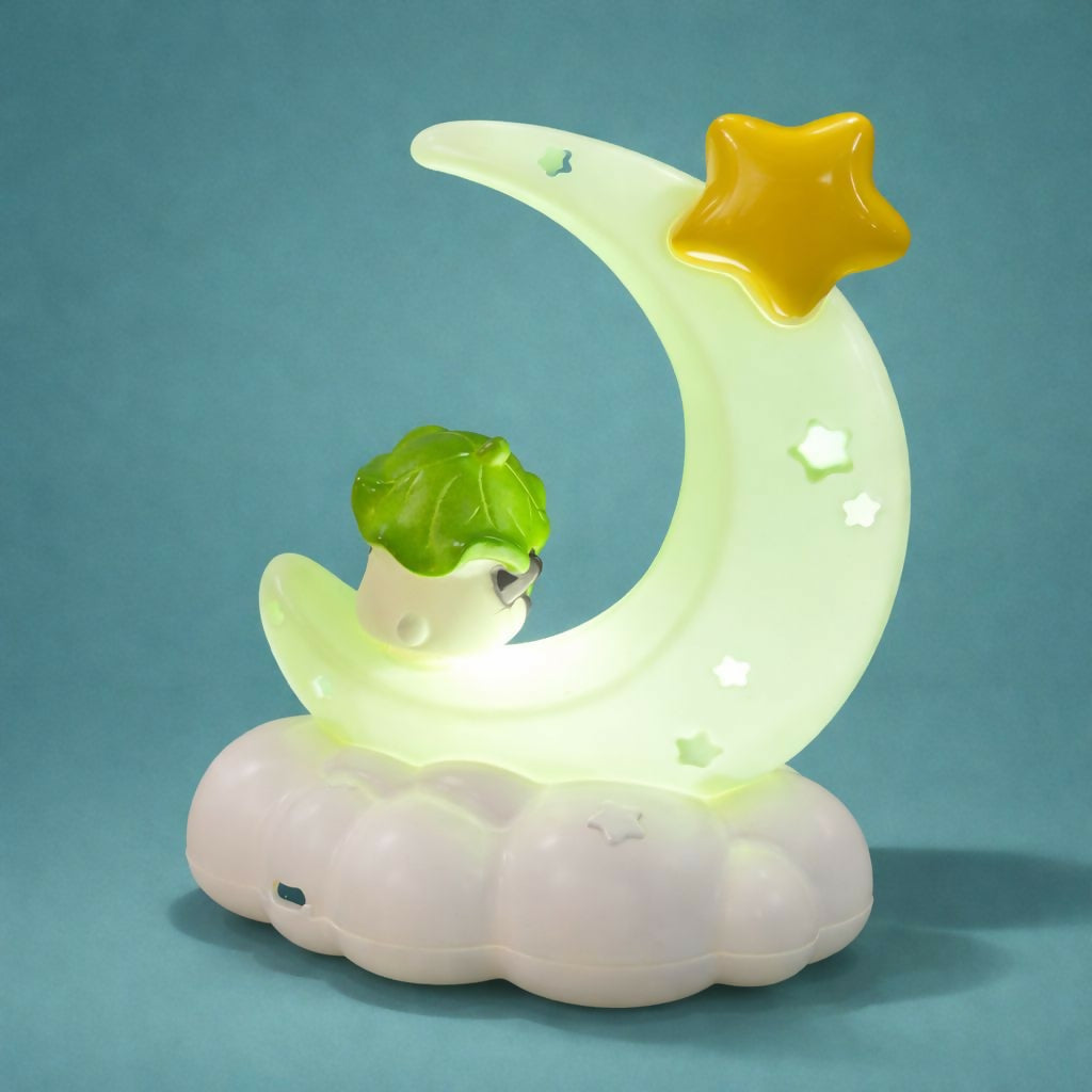 A glowing green crescent moon night light with a small character and star, on a cloud base against a teal backdrop.