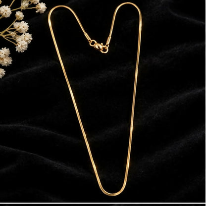 A delicate gold-tone snake chain necklace with a lobster clasp closure is displayed on a dark velvet surface.