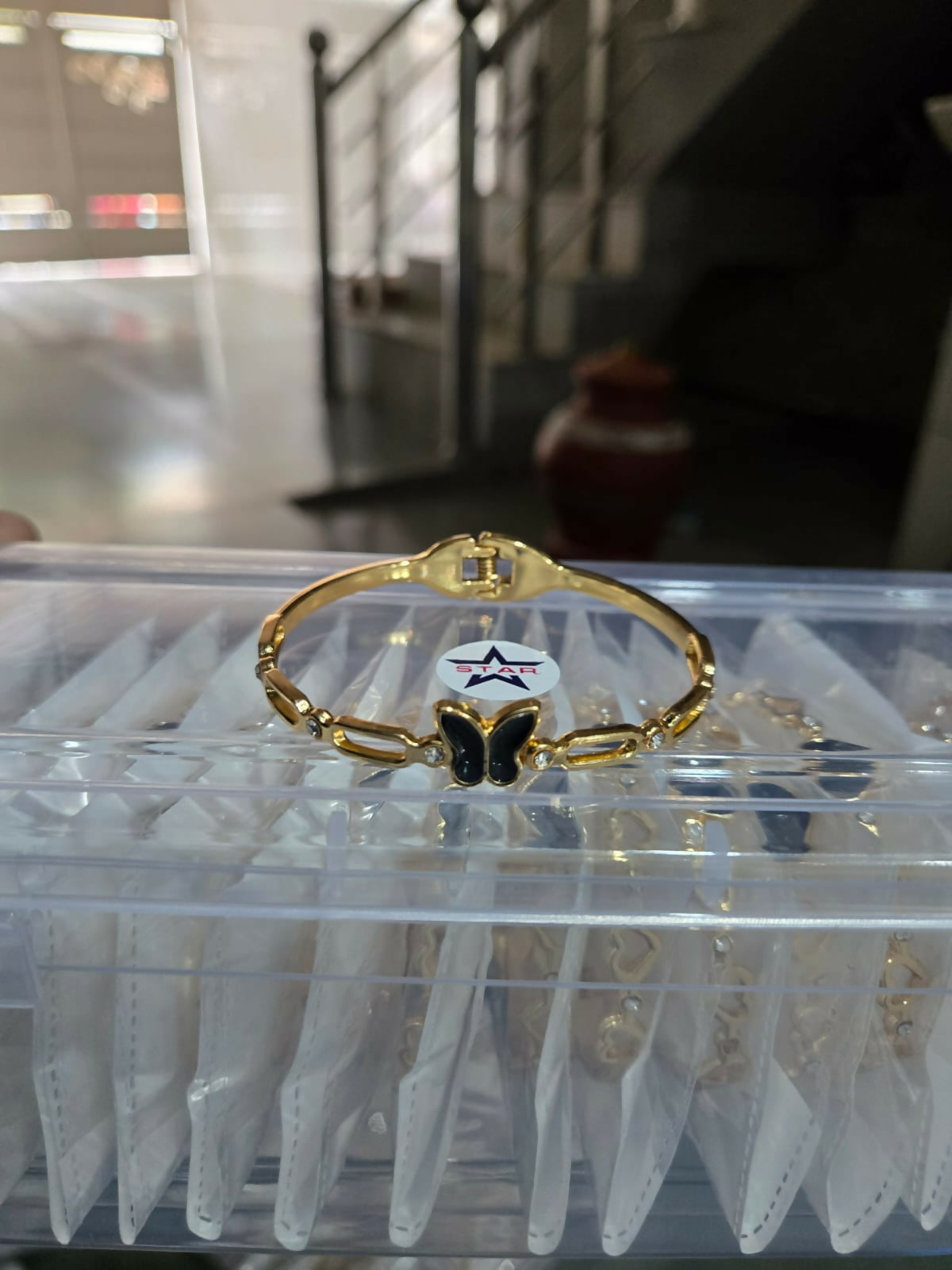 A gold-tone bracelet with a black butterfly charm and crystal accents is shown in a clear plastic case.