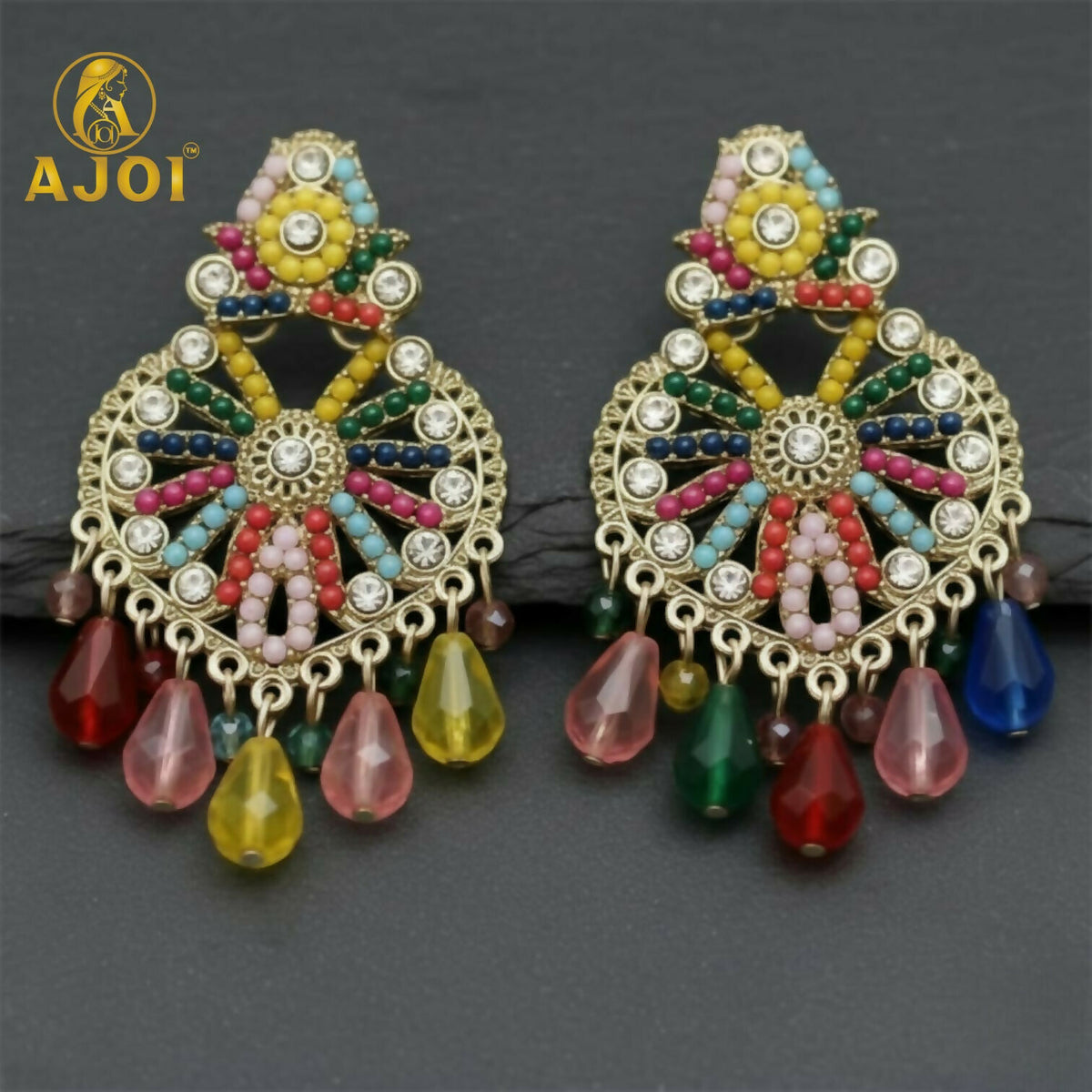 Two matching gold earrings with a central floral design, surrounded by colorful beads and clear stones, on a dark surface.