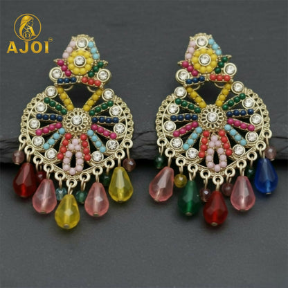 Two matching gold earrings with a central floral design, surrounded by colorful beads and clear stones, on a dark surface.