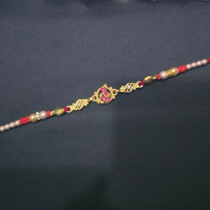 A gold and pink Lord Krishna Rakhi with red and white beads is centered on a plain black background.