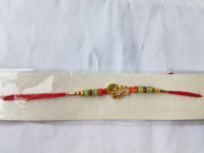 A red thread with a gold and green peacock charm, orange and mint green beads, and gold accents, is displayed horizontally