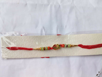 A red and gold bracelet with a peacock charm, orange and light green beads, and blue accents, packaged in clear plastic on
