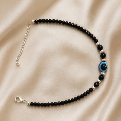 Black evil eye beaded anklet pair with a blue charm on a white background.