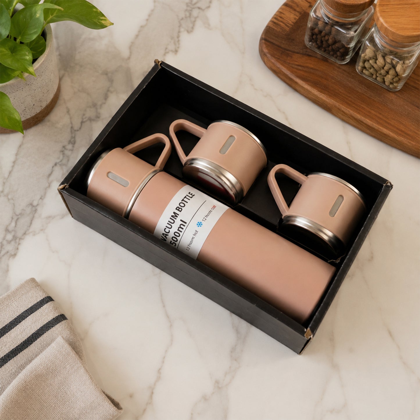 A pink vacuum flask and two matching cups are neatly arranged in a black gift box on a marble surface.
