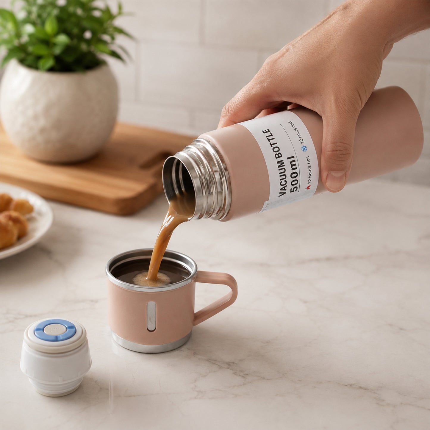 A hand pours coffee from a pink vacuum flask into a matching cup, with a small white speaker and green plant in the