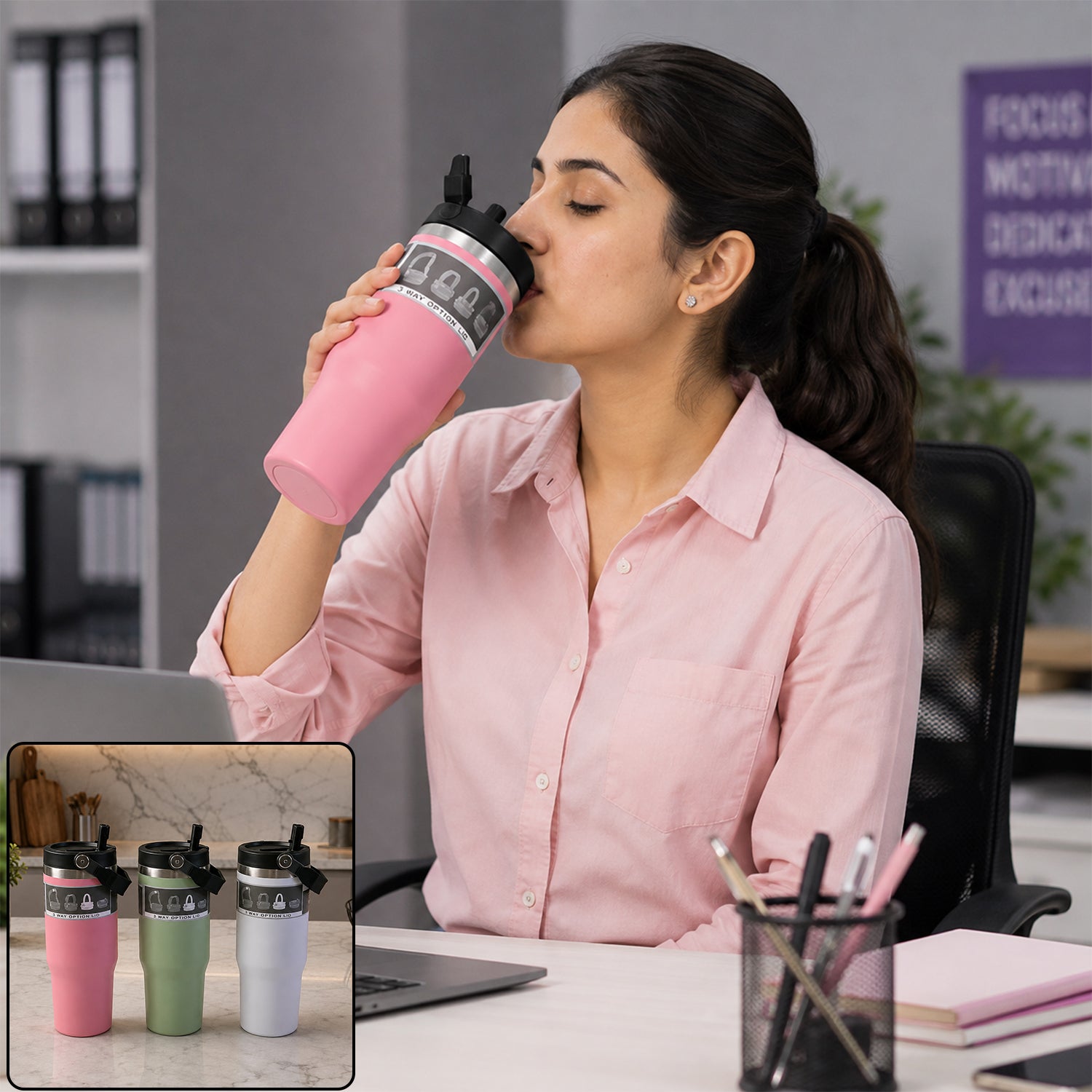 A woman in a pink shirt sips from a pink insulated tumbler with a handle at an office desk.