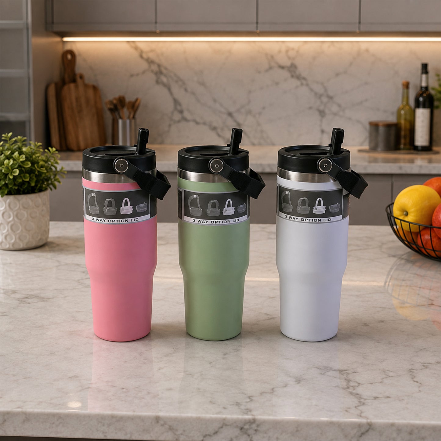 Three insulated tumblers in pink, green, and white with handles sit on a marble kitchen counter.