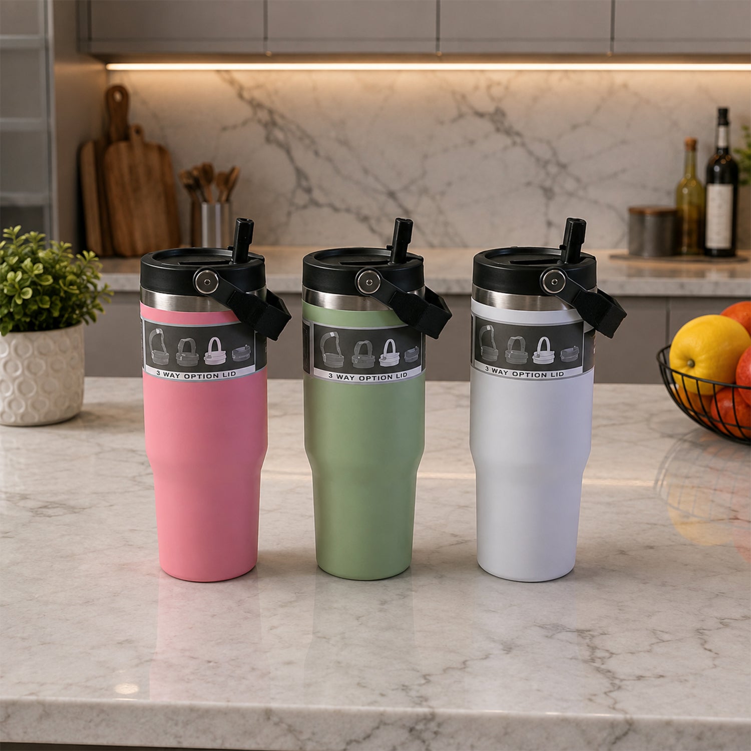Three insulated tumblers in pink, green, and white with handles sit on a marble kitchen counter.