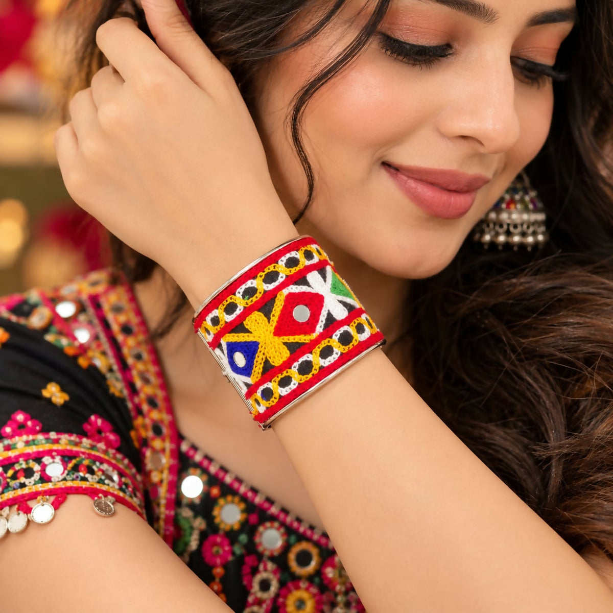 A woman wears a colorful embroidered cuff bracelet with mirror accents on her right arm.