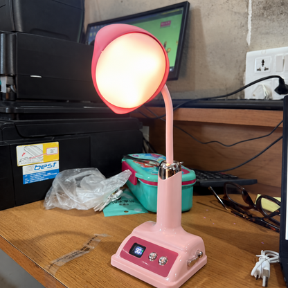 A pink desk lamp with a glowing light illuminates a cluttered wooden desk with a printer, keyboard, and other items.