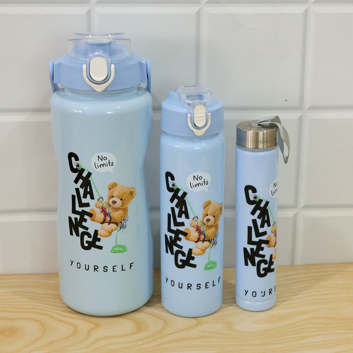 Three light blue water bottles with teddy bear graphics on a wooden surface against a white tiled wall.