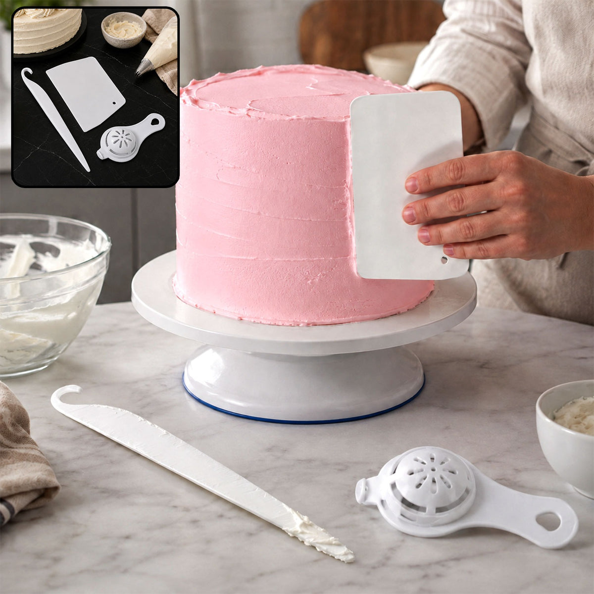 A person uses a white plastic scraper to smooth pink frosting on a cake on a white rotating stand, with other tools nearby.