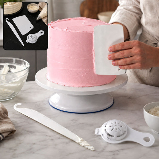 A person uses a white plastic scraper to smooth pink frosting on a cake on a white rotating stand, with other tools nearby.