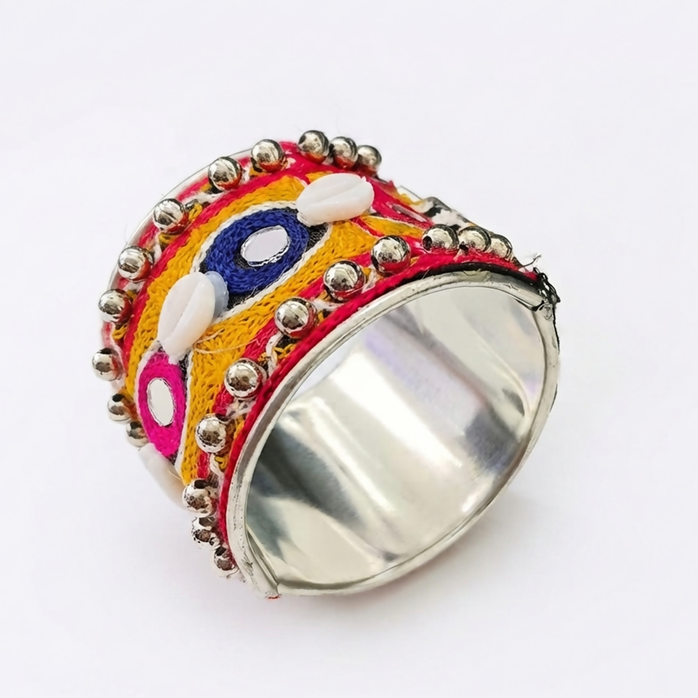 An angled view of the metal cuff bracelet, showcasing its shiny silver interior and colorful embroidered exterior with shell