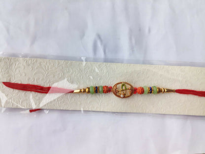 A red string bracelet with a central oval charm and colorful beads, packaged in clear plastic on a textured white card.