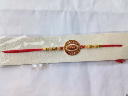 A red and gold bracelet with an oval centerpiece, pearls, and stones, is presented on a white textured card against a plain