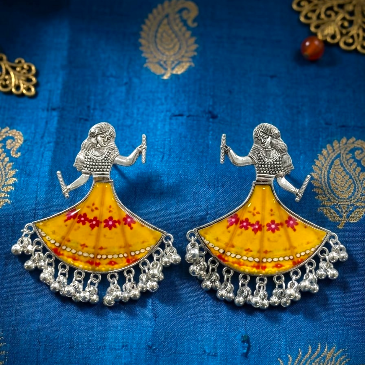 Two identical silver-toned earrings with yellow and red floral skirts, each adorned with tiny dangling ghungroos.