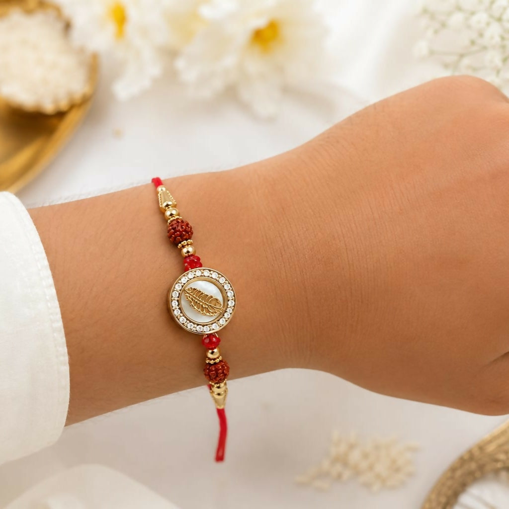 The golden feather dial with crystal halo and rudraksha accents is worn on a wrist, with a white shirt sleeve visible.