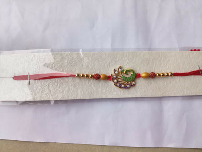 A red thread with gold beads and a central green and purple peacock design with white pearls is displayed on a textured