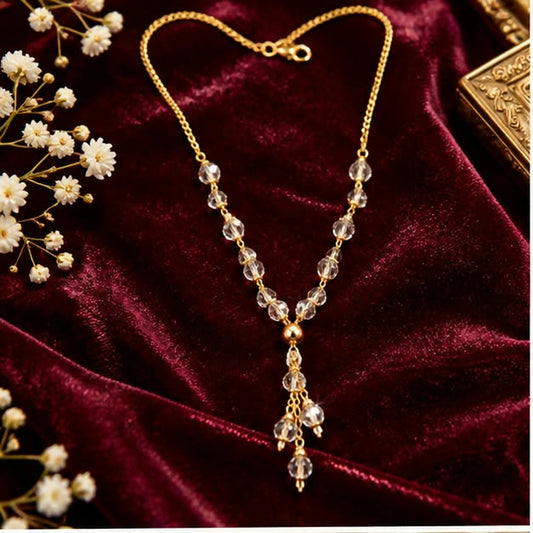 Gold chain Y-necklace with clear faceted beads and a triple drop pendant, displayed on a deep red velvet surface.
