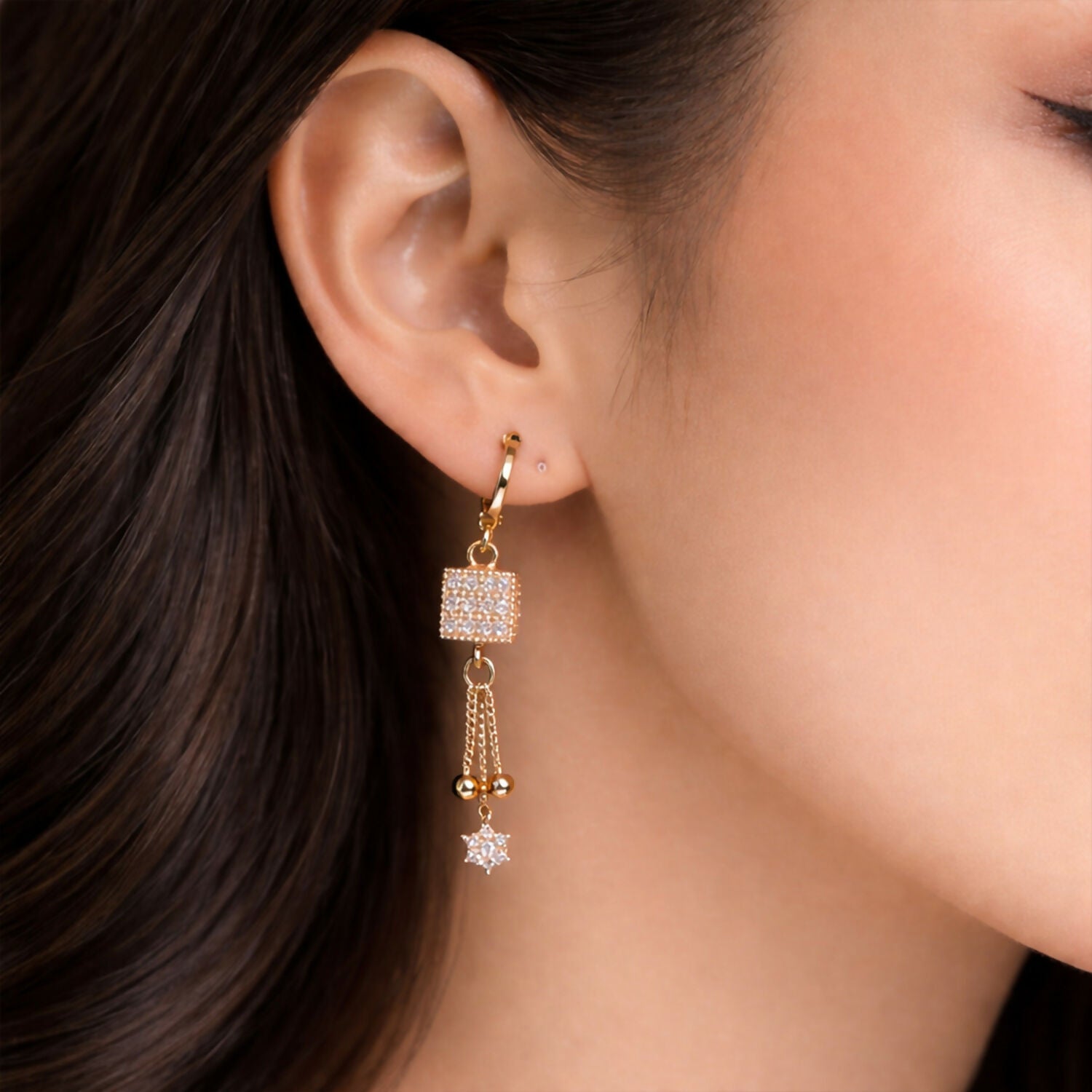 Close-up of sparkling square cube and delicate chain tassel on gold finish drop earrings