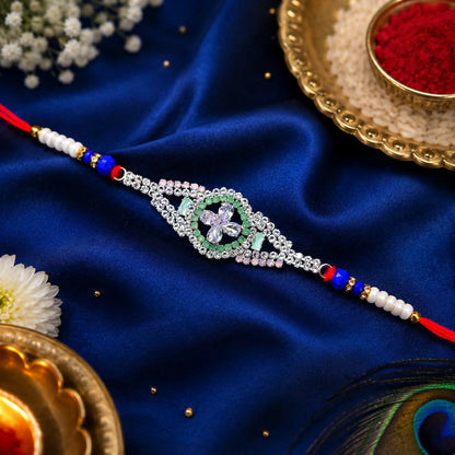 A silver-toned crystal flower design with green, pink, and clear stones on a red thread with white and blue beads, on a blue