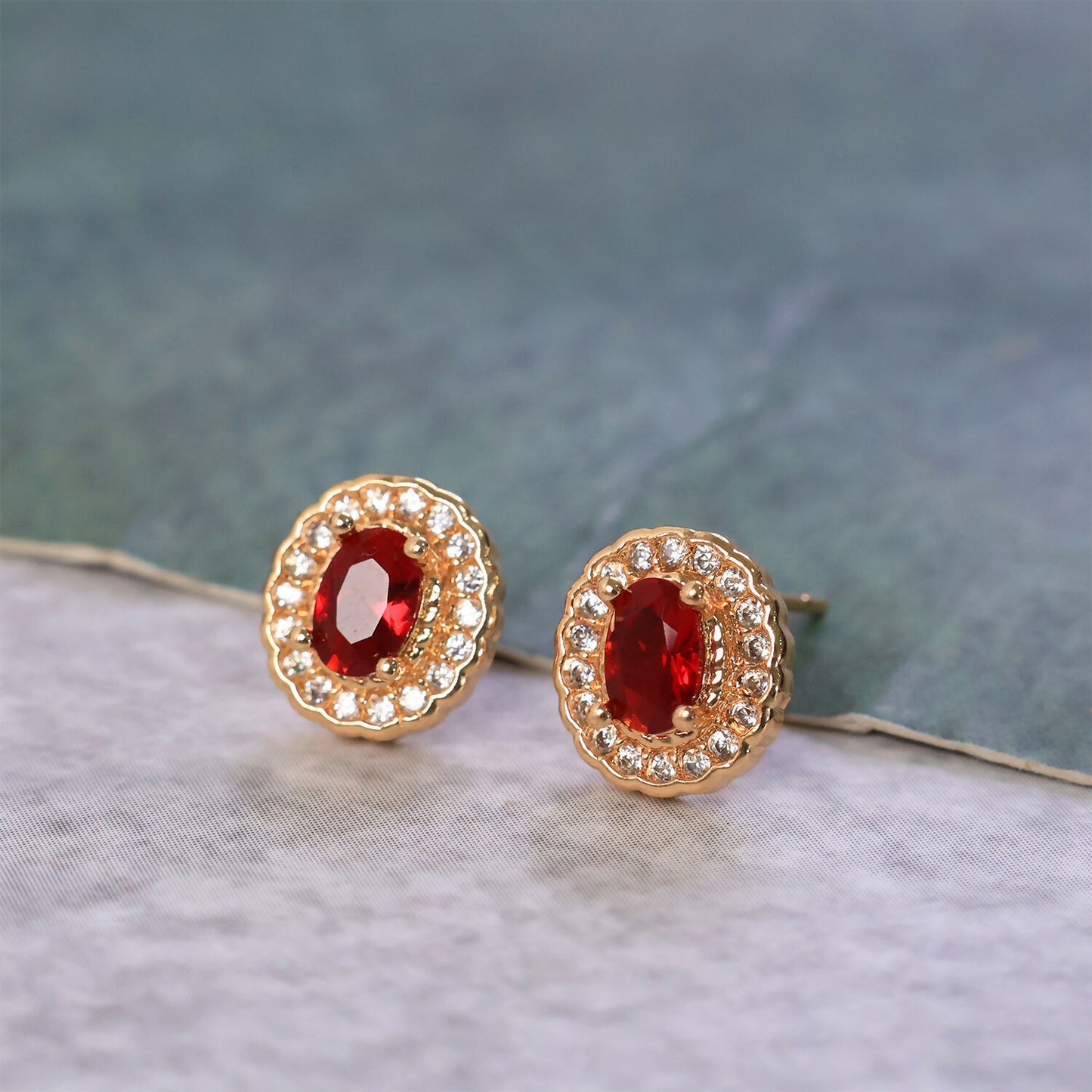 Close-up of oval red stone stud earrings with sparkling crystal halo design