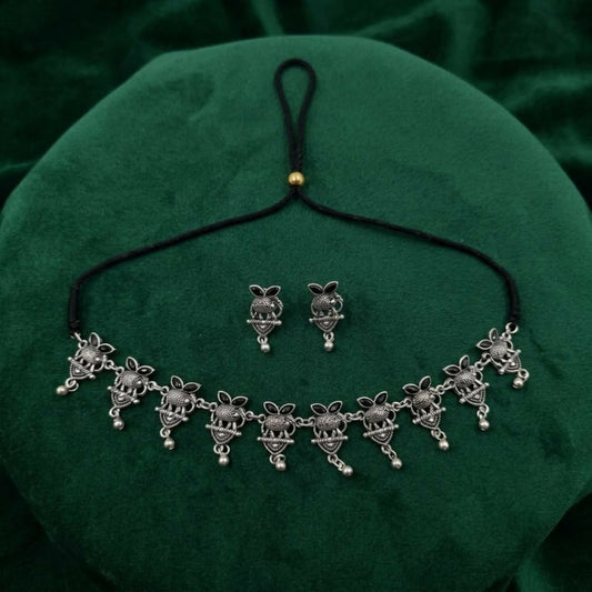 Oxidized silver tone choker necklace and matching earrings with black cord on a green velvet surface.