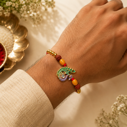 A man's wrist wears a festive thread with a peacock centerpiece, golden beads, and reddish-brown accents, against a