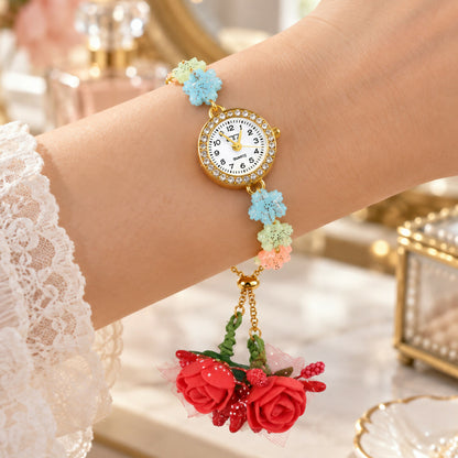 A woman's wrist displaying the watch with its colorful flower links and dangling red rose details.