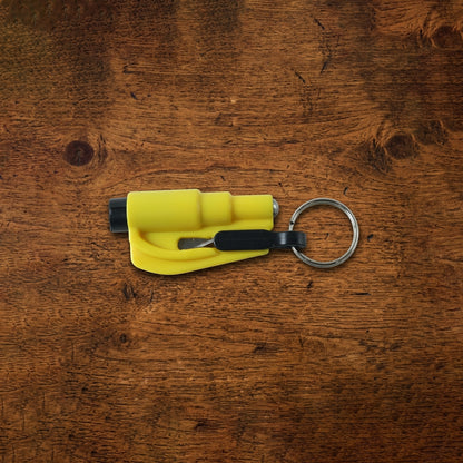 A yellow keychain car safety hammer with a black seat belt cutter and a silver key ring rests on a rustic wooden surface.