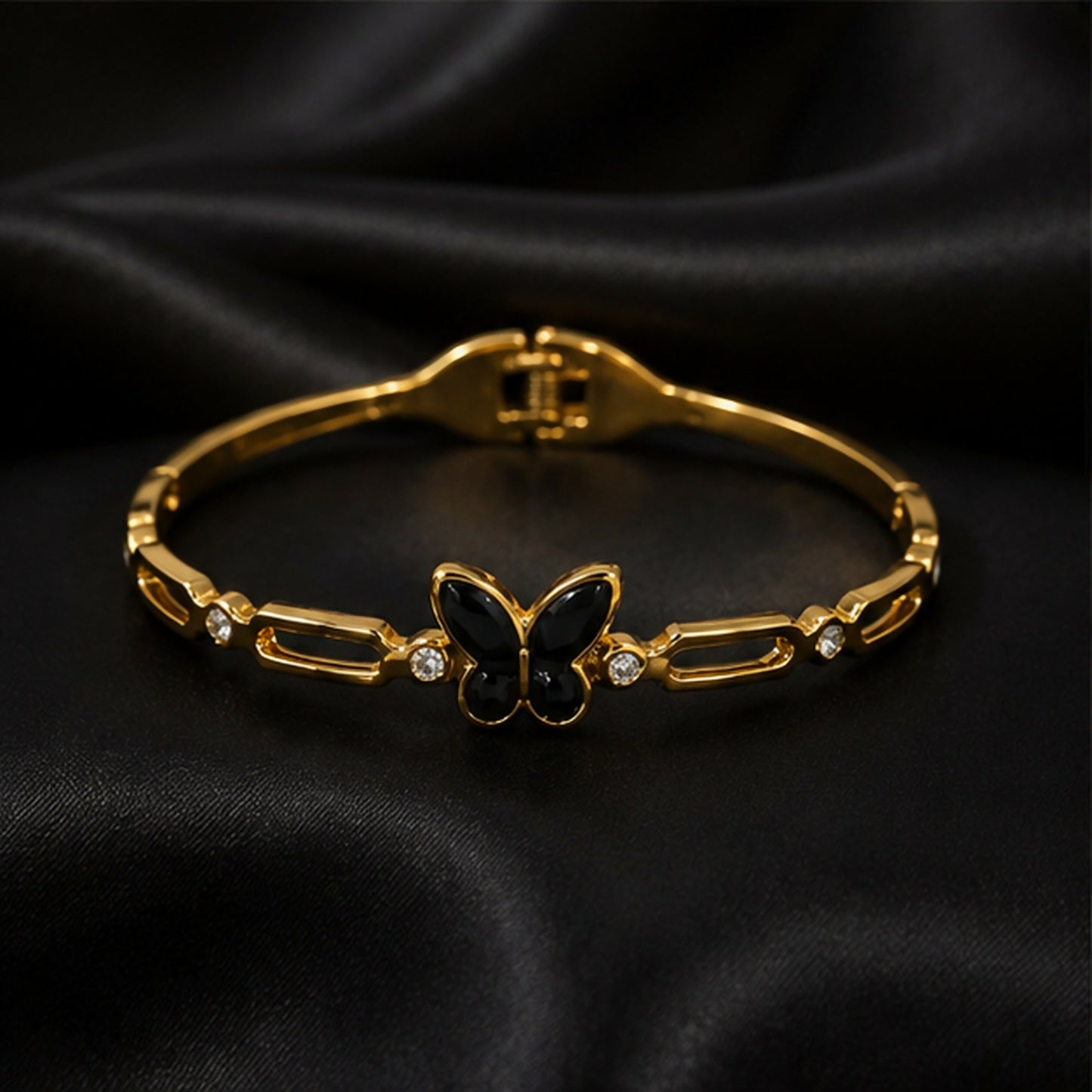 The gold-tone bracelet with a black butterfly charm and crystal accents is displayed on a black satin surface.