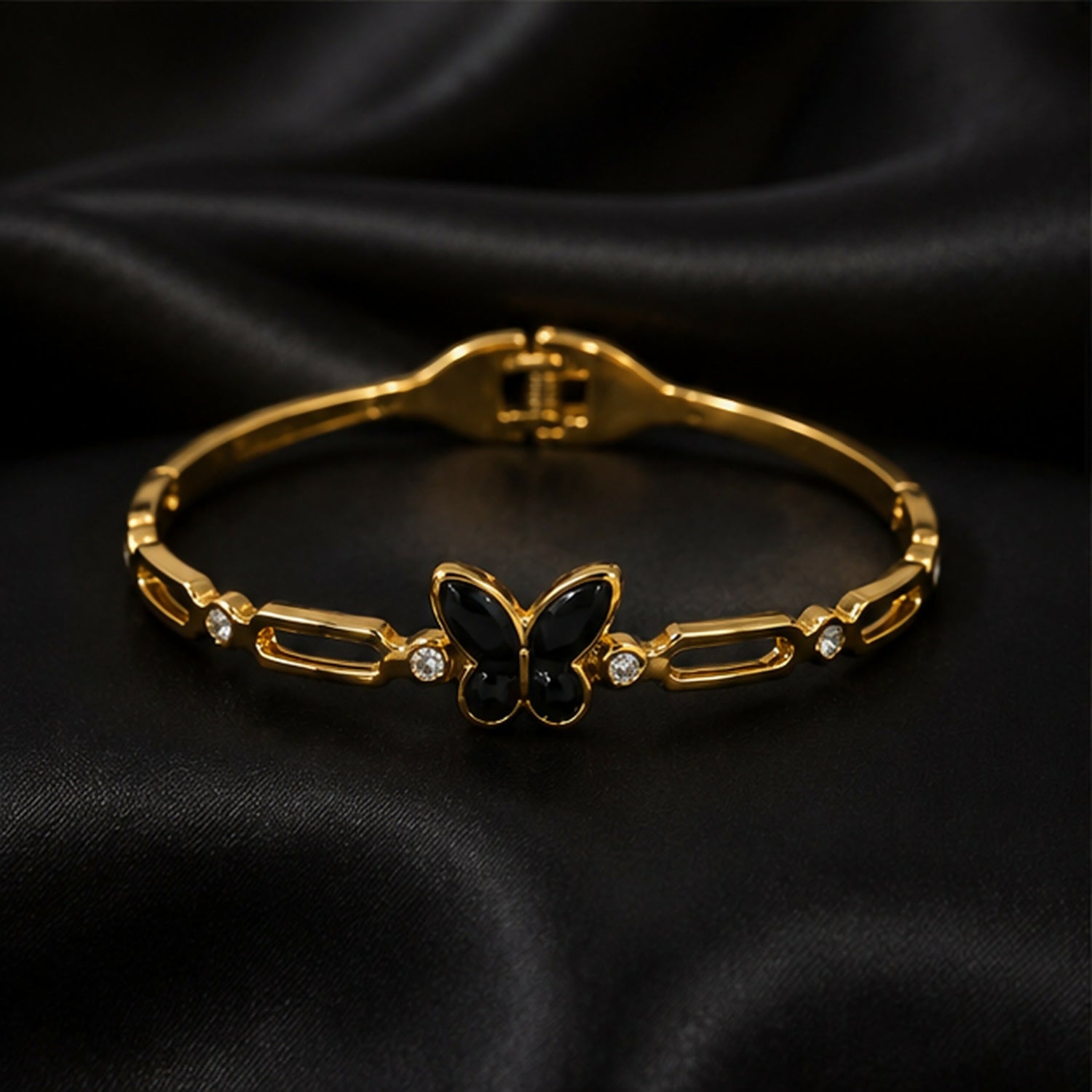 The gold-tone bracelet with a black butterfly charm and crystal accents is displayed on a black satin surface.