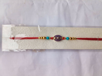 The red thread with a purple and gold oval charm, gold, and turquoise beads is displayed in clear packaging on a white