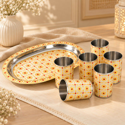 Six stainless steel glasses with a floral pattern and a matching oval serving tray on a table runner.