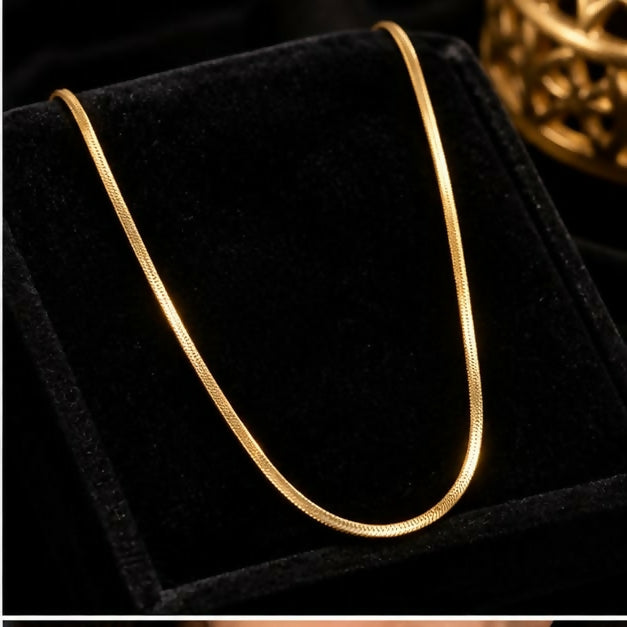 A lustrous gold-tone snake chain necklace is draped over a black velvet jewelry display stand.