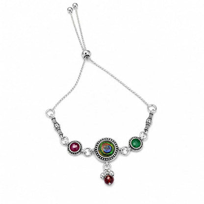 An antique silver adjustable bracelet with a peacock eye cabochon and maroon and green side stones is centered on a white