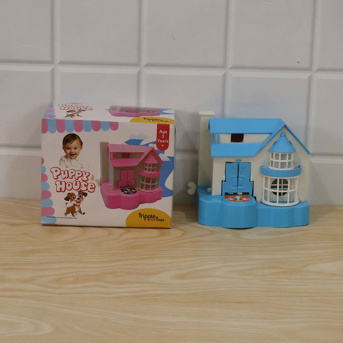 The blue and white house coin bank sits beside its pink and white retail packaging on a wooden surface.