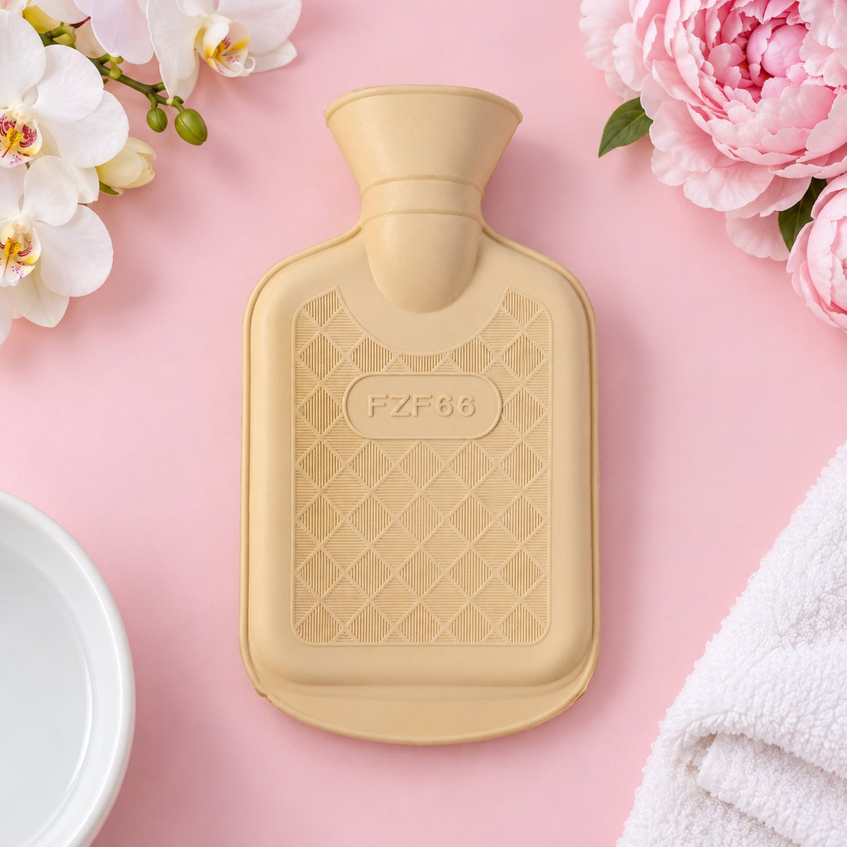 A cream rubber hot water bottle with a diamond texture sits on a pink surface with flowers.