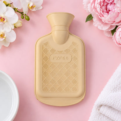 A cream rubber hot water bottle with a diamond texture sits on a pink surface with flowers.