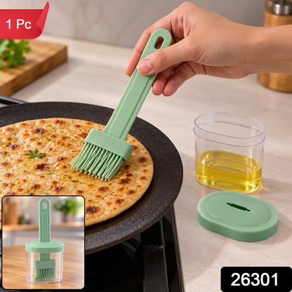 A hand uses a light green silicone basting brush on a cooking flatbread, with a clear oil container and a smaller inset